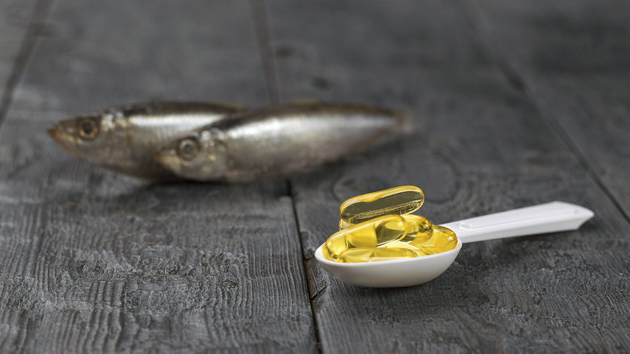 Buying Guide To Fish Oil Supplements by Superscoopz.com, features a spoon of fish oil capsules in the foreground with cod fish in the background